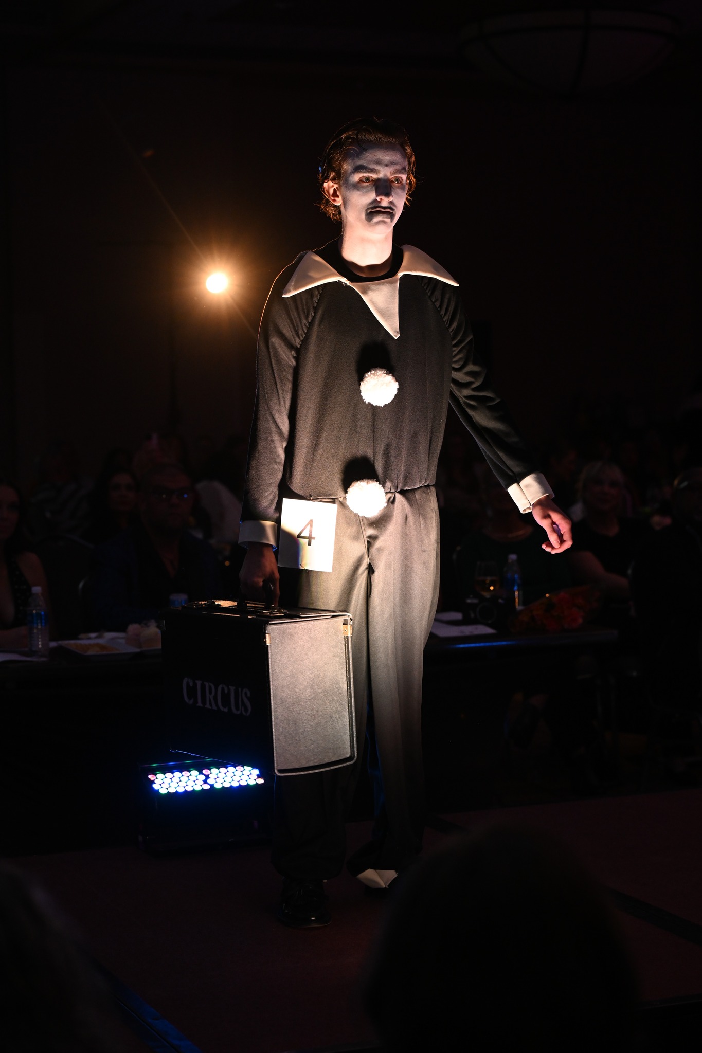 Model on the Project Funway runway wearing Noah Gumm's black and white Pierrot-inspired look with an oversized collar and pom-poms, carrying a Circus case.